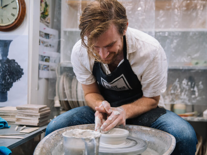 A dad laughs as he learns wheel throwing